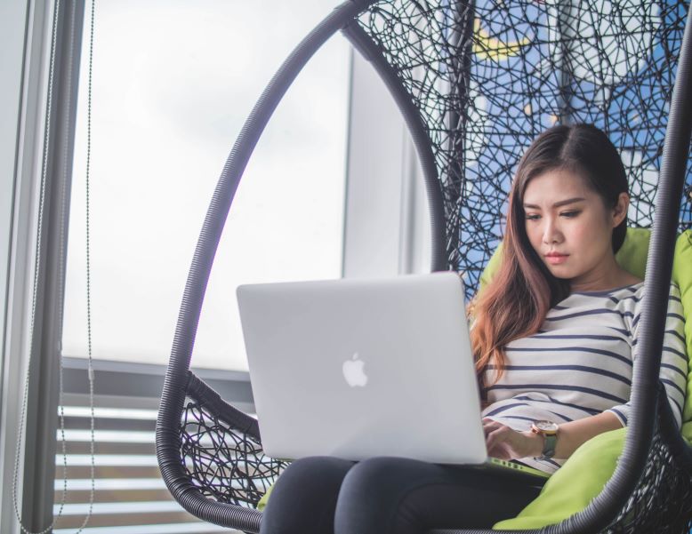 woman sitting in hanging chair typing on computer